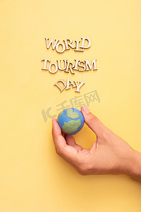 旅游海报设计摄影照片_世界旅游日文字，黄色背景上的木字，女性手中的地球仪顶视图