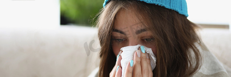 戴着温暖帽子、盖着毯子的妇女用纸巾擦湿流鼻涕