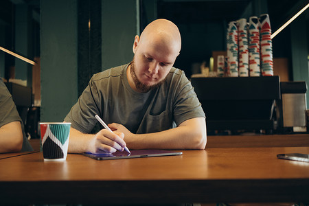 穿着休闲服的年轻创意网页设计师一边工作一边喝咖啡和饼干，在平板电脑上用手写笔画画