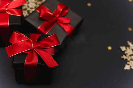 黑色礼品盒，金色五彩纸屑背景上有一条红丝带。