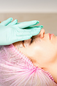 戴着手套的美容师在女性脸上涂上带去角质霜的保湿面膜。