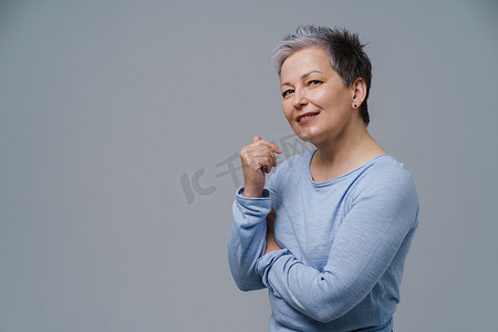 灰白的头发摄影照片_50 多岁的成熟女性，头发灰白，双手交叉，左侧复制空间，背景为白色。