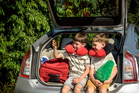 两个可爱的小孩男孩在离开去暑假前坐在汽车后备箱里。