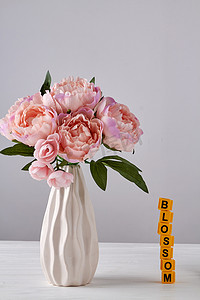 花瓶中的牡丹花摄影照片_白色花瓶中的粉红色牡丹花在白色背景上。