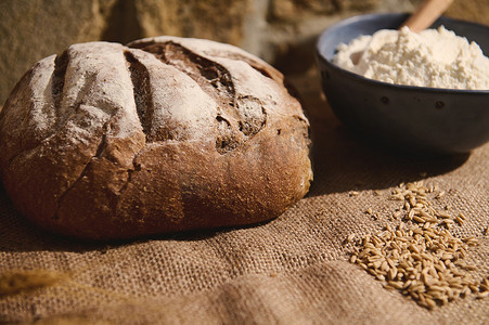 在粗麻布桌布上放着新鲜出炉的酵母小麦面包、麦穗和烘焙配料的静物生活