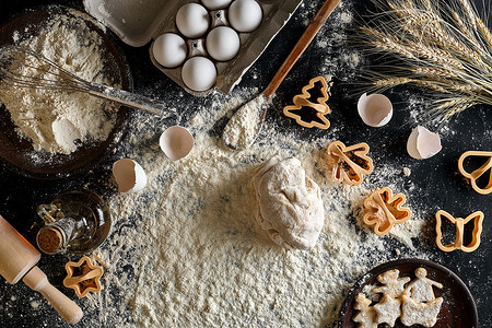 鸡蛋烹饪摄影照片_黑桌上的饼干、黄油、鸡蛋、烹饪设备、面粉的烹饪面团。