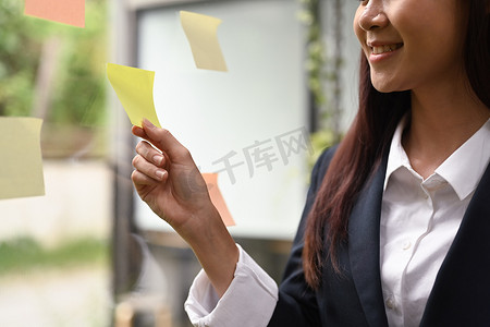 微笑的亚洲女经理在玻璃墙上的粘纸上阅读信息或想法的剪影