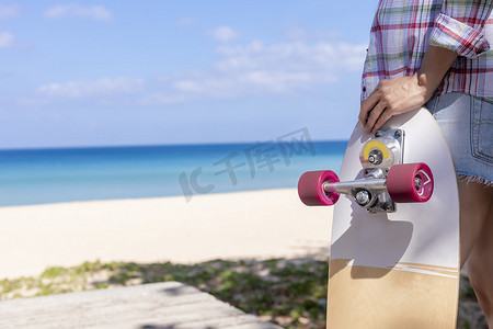 特写年轻女性拿着有海滩背景的冲浪滑板。