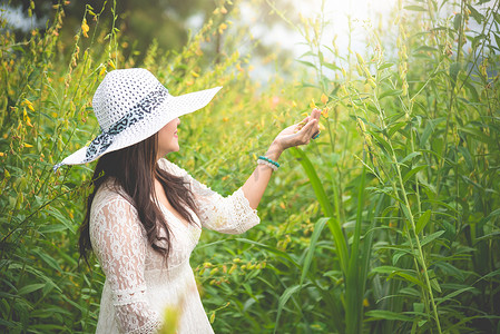 身穿白色连衣裙、头戴翼帽的亚洲美女在油菜花田背景中行走。