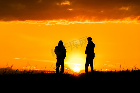 两个男人在日落或日出时与戏剧性的天空和云交谈的剪影。对话和在地平线和天际线上遇见两个人。阳光下的人的轮廓。与朋友的黄金时光