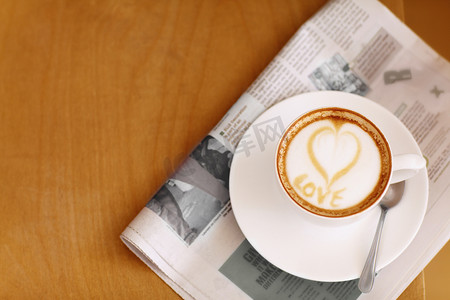 咖啡爱好者摄影照片_用爱制作...高角度拍摄的一杯精心准备的卡布奇诺放在报纸上。