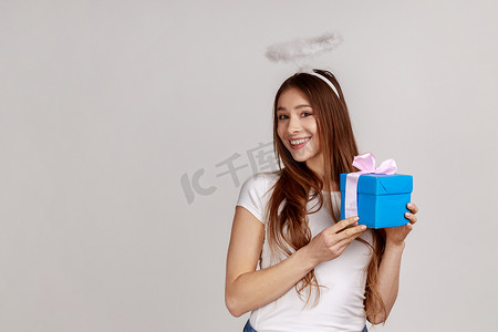 天使般的年轻女子，带着光环，拿着礼物盒，对着镜头微笑，对礼物感到满意。