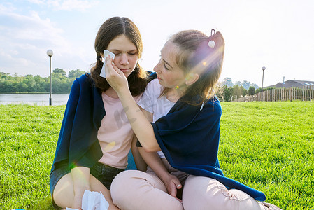 哭泣的少女和安慰女朋友，青少年坐在公园的草地上