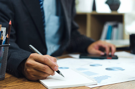 商人拿着笔写书和文档图表会计财务论文工作分析图表营销投资和报告经济在办公室的办公桌上。