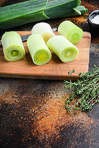 有机切碎的韭菜，用于在木板上用香草配料烹制红烧韭菜，在质朴的金属背景下，深色，侧视。
