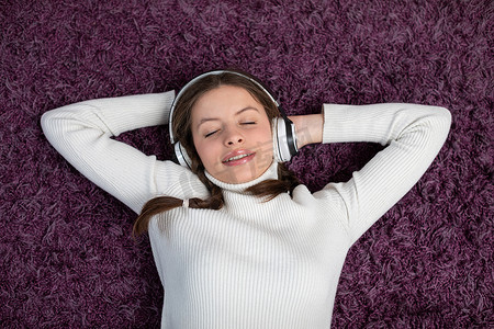 一名微笑的青少年躺在菲力地毯上，戴着耳机听音乐。