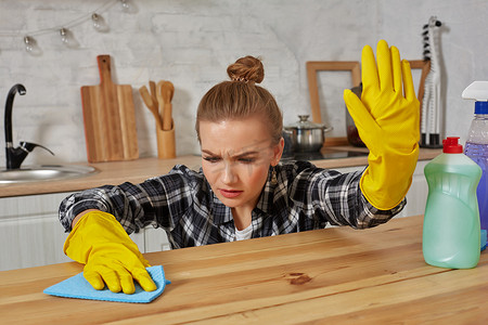 戴着防护手套的年轻女人用抹布擦厨房的桌子
