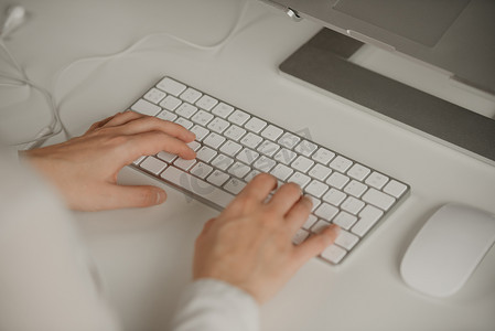 女性双手在无线白色铝制键盘上打字的特写照片。