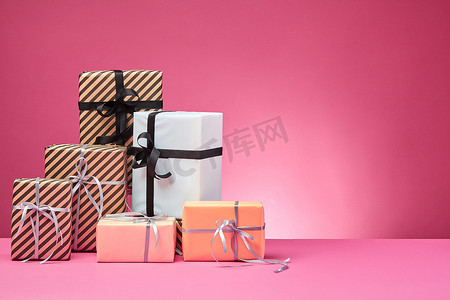丝带感恩背景摄影照片_不同尺寸、彩色、条纹和普通纸质礼盒，在粉红色的表面和背景上绑着丝带和蝴蝶结。