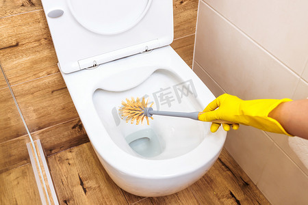 动漫厕所摄影照片_特写，一只戴着黄色手套的女手拿着一个装在蓝色瓶子里的厕所清洁剂