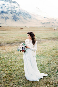 新娘穿着白色的裙子，在绿色的牧场上捧着一束花。