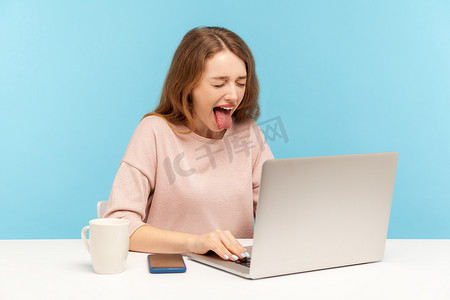 在蓝色背景上使用笔记本电脑的情感年轻女子。