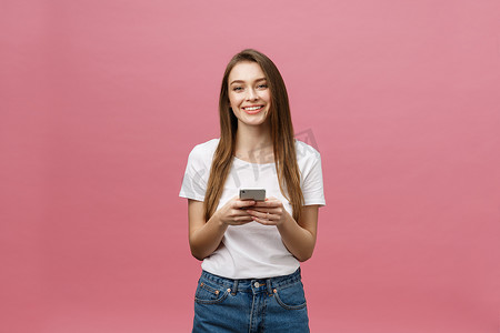 一张欢快可爱的美丽年轻女子在粉红色墙壁背景下用手机聊天的照片。