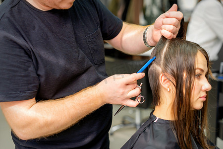 线条分割摄影照片_美发师将女性头发分成几部分，用梳子在美发沙龙特写中用手握住头发。