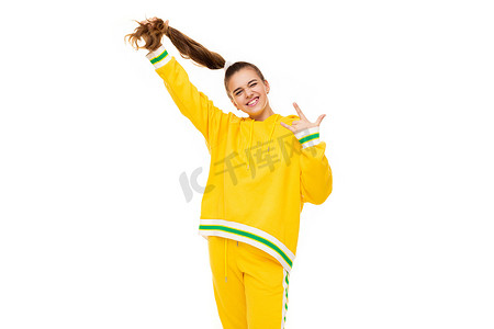 照片中一位美丽的微笑女孩留着深色头发，身着带绿色条纹的时尚黄色运动服，扎着马尾辫，照片上的岩石手在白色背景中被隔离，并有可用的文字空间