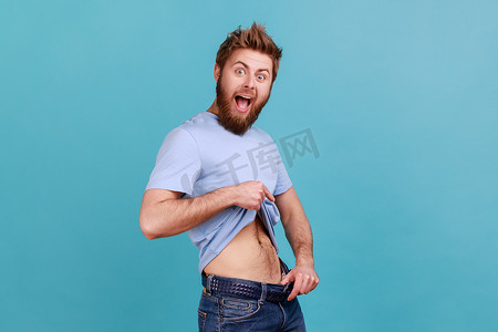 减肥成功摄影照片_穿着蓝色 T 恤的男人穿着大裤子，腰部纤细，减肥成功。