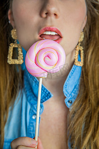 一个漂亮女孩的肖像，蓝色背景上有彩色粉色旋转棒棒糖硬糖、糖果、糖和不健康食品的概念