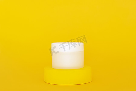 白色无品牌化妆品霜罐站在黄色讲台上。