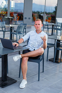 一位成功的年轻主管在酒店露台的笔记本电脑桌前工作，并在异国情调的度假胜地度假时抽出时间远程管理员工。