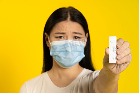 手握相机摄影照片_戴着医用口罩、手握测试的亚洲女性悲伤地看着黄色背景中孤立的相机。