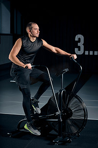 健身男性在功能训练馆使用空气自行车进行有氧运动。