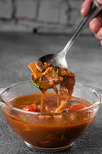 汤用肉、蘑菇、西红柿在灰色背景的透明碗里。