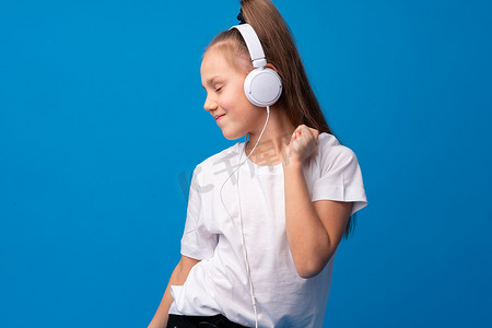 小女孩戴耳机在蓝色背景下听音乐
