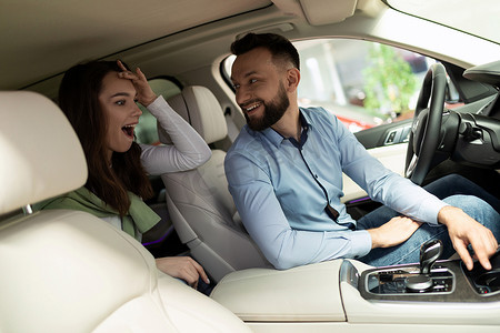 秋季促销活动海报摄影照片_汽车经销店的一男一女坐在车内，对新技术和促销活动感到惊讶