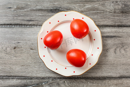 白盘上的三个完整西红柿，上面有小红点和金色边缘，灰色木桌，桌面视图。
