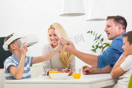快乐的白人家庭在家里的餐桌上，用虚拟现实耳机玩游戏