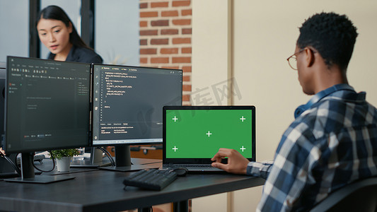 数据库设计人员使用带有绿屏色度键模型的笔记本电脑编写代码，坐在办公桌前