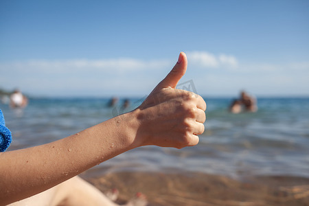 女性手竖起大拇指在海和天空背景特写。