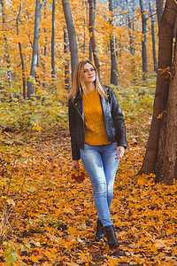 女孩抱着落叶，在秋天的公园里散步。