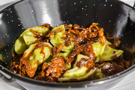 坚果酱摄影照片_蔬菜饺子配焦糖洋葱和坚果酱，放在白色木制背景的黑色碗里。