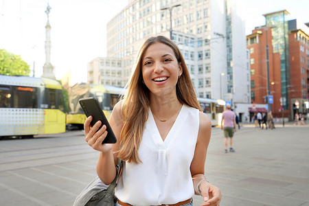 动态背景城市摄影照片_有魅力的商业女性拿着智能手机看着城市背景下的相机。