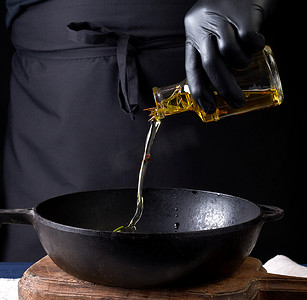 倒油瓶摄影照片_戴着黑色乳胶手套的厨师从透明的瓶子里倒橄榄油