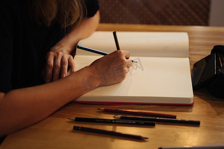 素描本摄影照片_一个女孩坐在咖啡店里，用彩色铅笔在素描本上画画。