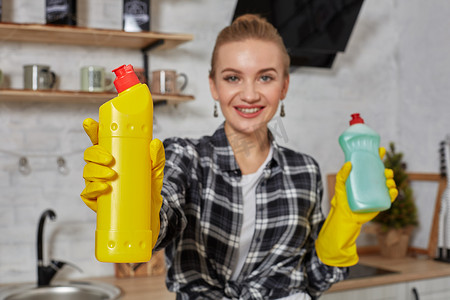 女人比较洗涤剂产品，她拿着两个瓶子，在家里的厨房里检查它们。