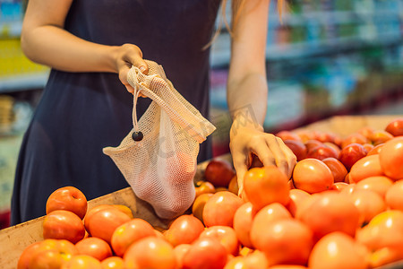 一名妇女在超市挑选西红柿，没有使用塑料袋。