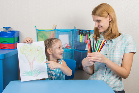 照片上的五岁女孩看着手里拿着彩色铅笔的母亲